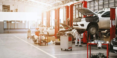 Large automotive repair facility with cars lifted on hydraulic lifts, mechanics working, and bright open workspace prepared for painting services.
