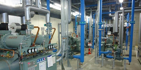 Cold storage facility interior with blue-painted pipes, machinery, and refrigeration equipment in a clean industrial space.