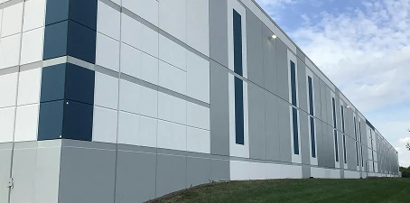 Exterior wall of a modern industrial facility with geometric paint patterns in gray, white, and blue panels.