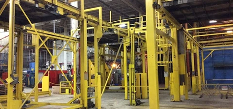 Interior of a manufacturing plant with yellow steel framework, industrial equipment, and open workspace for production processes.