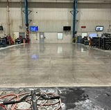 Industrial warehouse floor with a high-gloss finish after concrete polishing, reflecting lights and equipment along the walls.