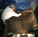 Worker in protective gear using dry ice blasting equipment to clean industrial machinery components.