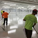 Workers applying epoxy flooring in a large industrial facility, creating a smooth, glossy surface under bright overhead lights.