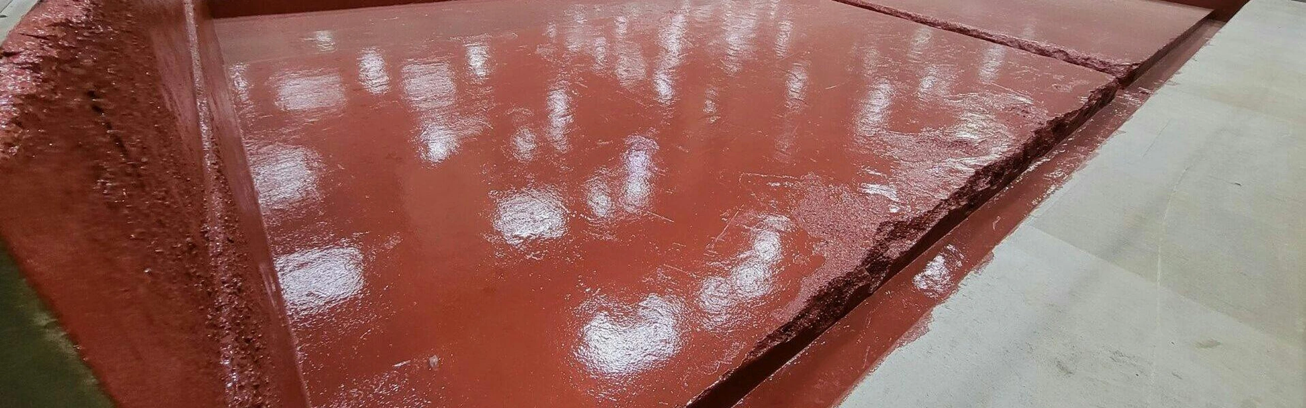 Close view of thick red epoxy/urethane floor topping with a roughened edge and visible expansion joint.