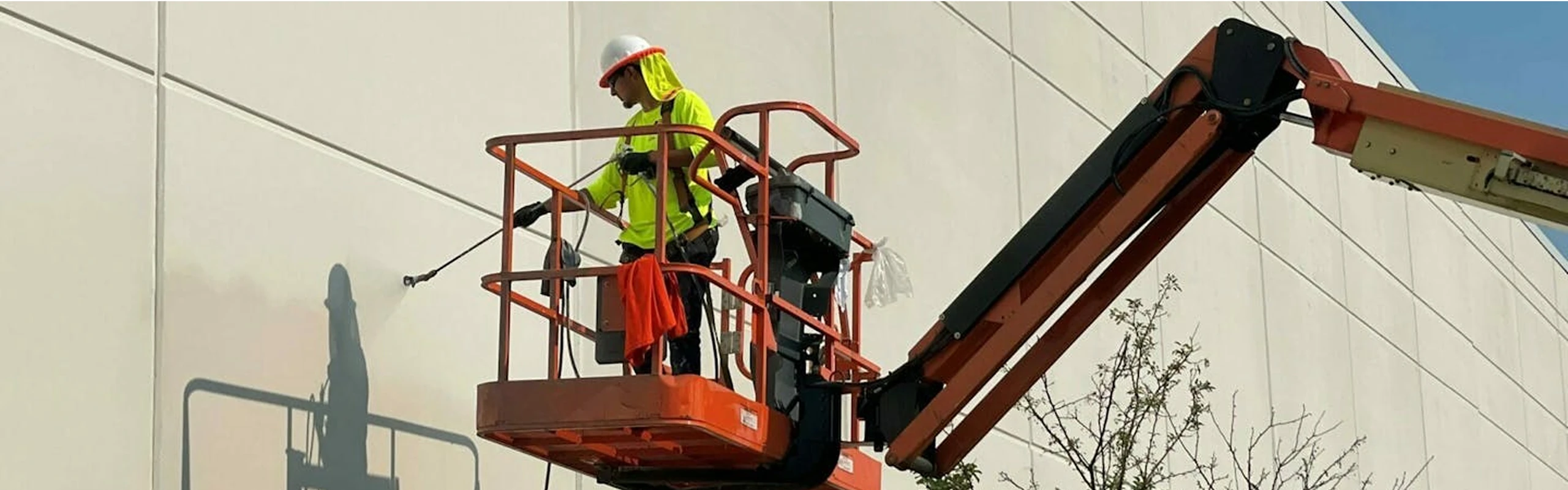 Worker in safety gear on a boom lift spraying and painting the exterior wall of a large commercial building.