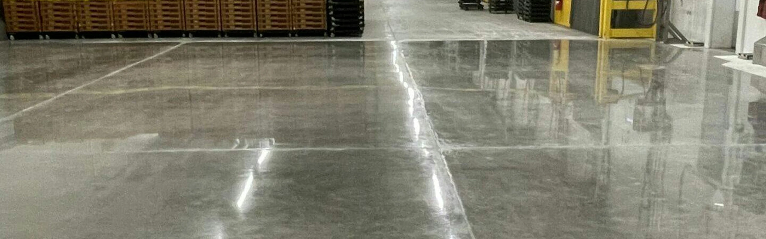 Highly polished warehouse floor reflecting overhead lights between pallet stacks and production equipment.