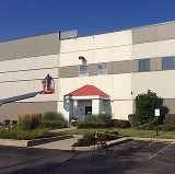 Commercial tilt-up concrete building exterior being painted, with a worker on a lift applying fresh coating to upper walls.