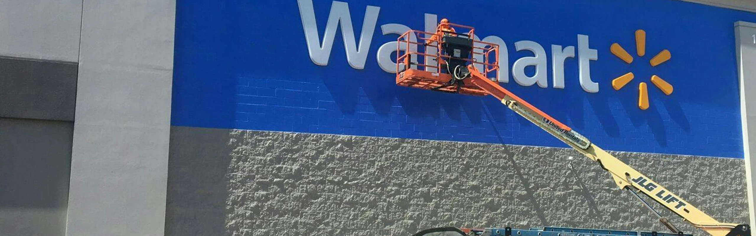 Worker on a boom lift painting the blue exterior wall of a Walmart store near the large white logo.